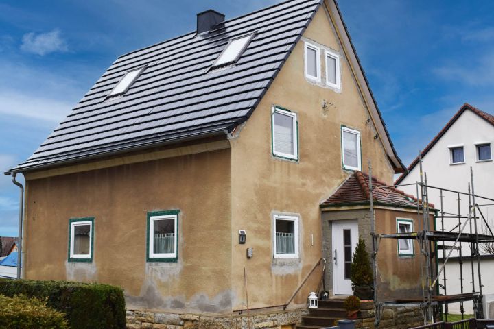 Ein zweistöckiges Haus mit brauner Fassade und schwarzem Dach, Gerüst an der Seite.